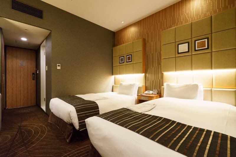 Phòng đôi giường đơn trong Sotetsu Fresa Inn Higashi Shinjuku, Tokyo, Nhật Bản, với đầu giường có đệm và đèn dải phía trên gối, thảm nâu với hoa văn hình xoắn ốc Phòng đôi giường đơn trong Sotetsu Fresa Inn Higashi Shinjuku, Tokyo, Nhật Bản, với đầu giường có đệm và đèn dải phía trên gối, thảm nâu với hoa văn hình xoắn ốc