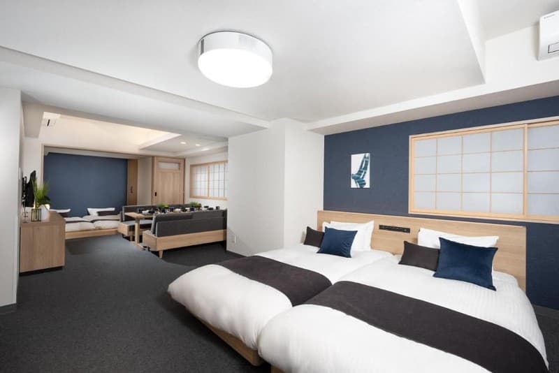 Phòng gia đình trong khách sạn Mimaru Tokyo Shinjuku West, Tokyo, Nhật Bản, với hai bộ giường đôi, bàn ăn dài với chỗ ngồi sofa, và thiết kế đương đại cập nhật từ phong cách tối giản truyền thống Nhật Bản Phòng gia đình trong khách sạn Mimaru Tokyo Shinjuku West, Tokyo, Nhật Bản, với hai bộ giường đôi, bàn ăn dài với chỗ ngồi sofa, và thiết kế đương đại cập nhật từ phong cách tối giản truyền thống Nhật Bản